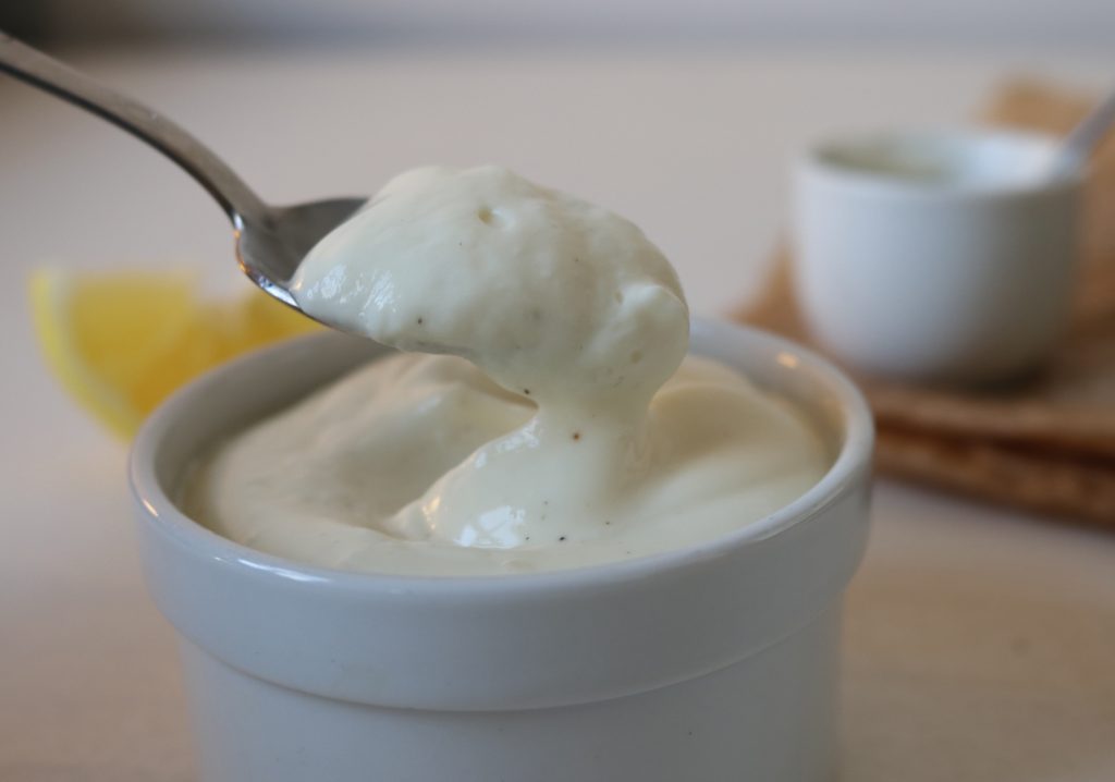 Vegane Mayonnaise in einer Schale. Ein Löffel holt etwas daraus heraus.
