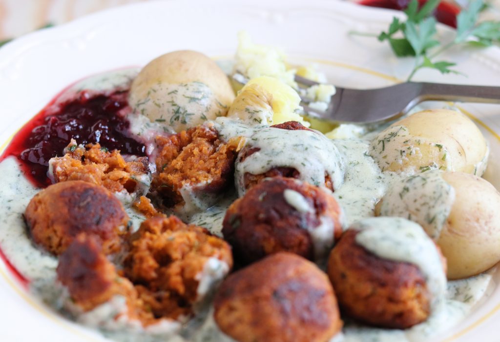 Vegane Köttbullar mit Dillsoße und Pellkartoffeln auf einem Teller. Zwei Bällchen sind in der Mitte zerteilt und man sieht das Innere.