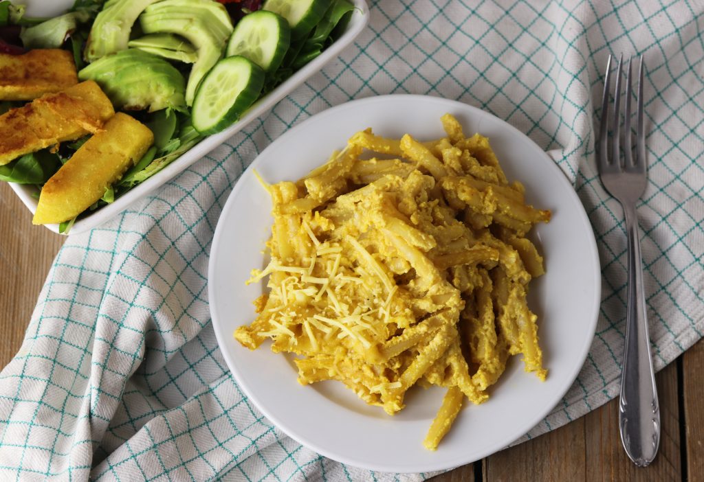 Vegane Mac'n'Cheese auf einem Teller, daneben eine Schale Salat