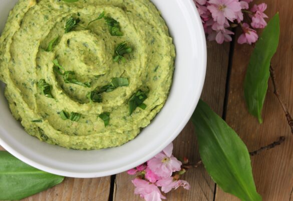 Bärlauchhummus – in einer weißen Schale. Daneben rosa Kirschblüten.