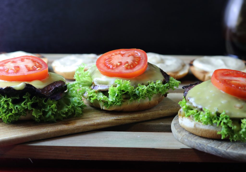 4. Die Brötchenhälften mit der Sauce bestreichen. Dann mit Salat, Portobellos mit veganem Käse, Roten Zwiebeln und Tomatenscheiben belegen.