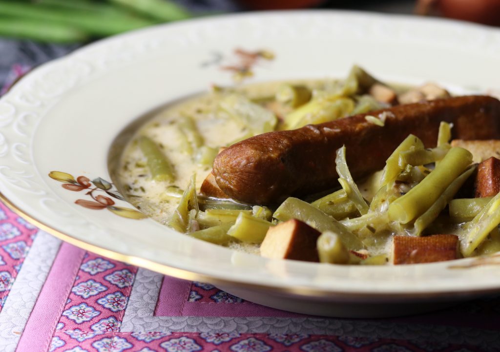 Schnippelbohnensuppe mit veganer Wurst in einem antiken Suppenteller serviert.
