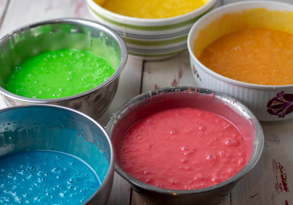 Bunte Biskuitteige, noch roh in Schalen, für eine Regenbogentorte.