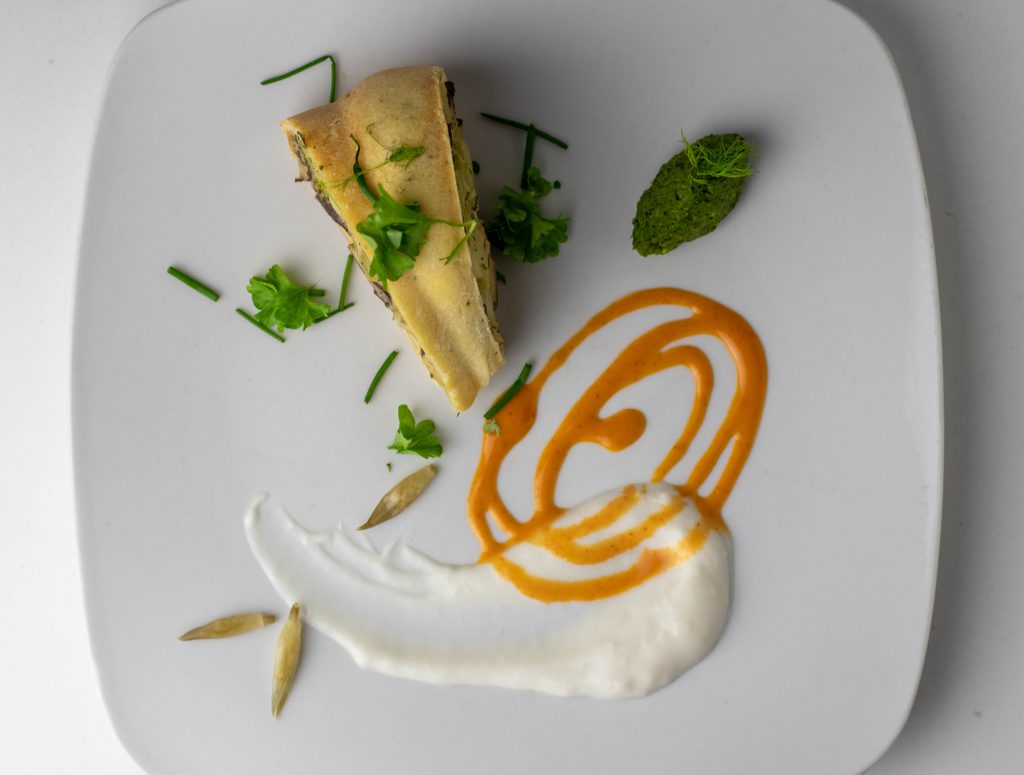 Ein Stück Pot Pie angerichtet mit scharfer Sriracha Mayo, veganem Joghurt, einer Nocke aus selbstgemachtem Bärlauchpesto und eingelegten Bärlauchkapern.