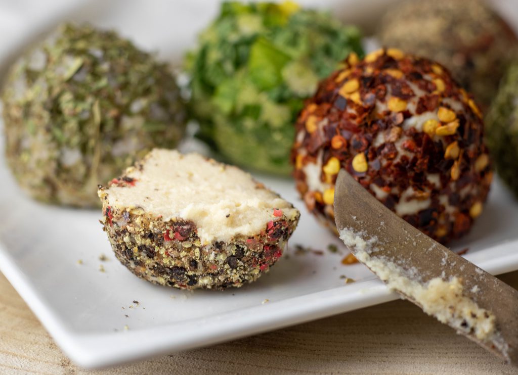 Vegane Frischkäsebällchen im Kräutermantel. Einer ist angeschnitten.