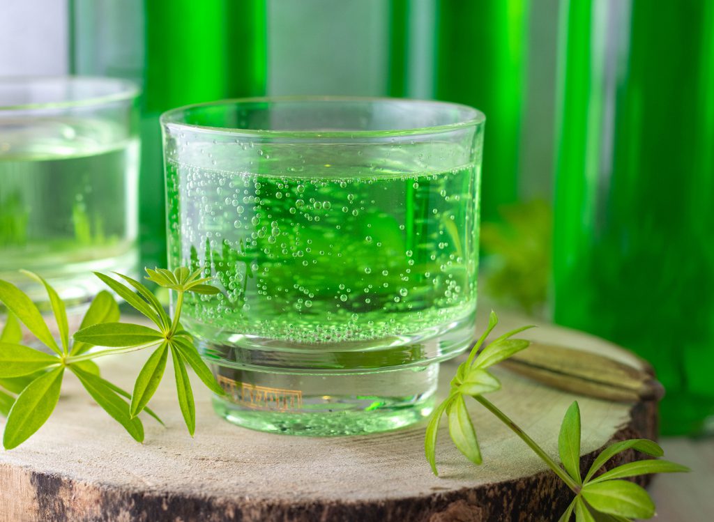 Waldmeistersirup in Sprudelwasser und in Flaschen