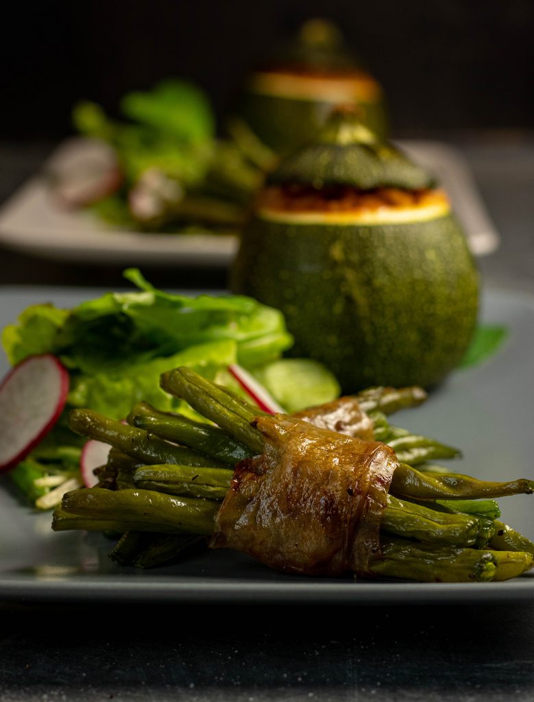 Gefüllte runde Zucchini, dazu Bohnen im veganen Speckmantel