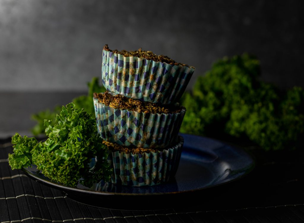 Grünkohl-Cupcakes in Papierförmchen. Gestapelt auf einem Teller. Dahinter frischer Grünkohl.