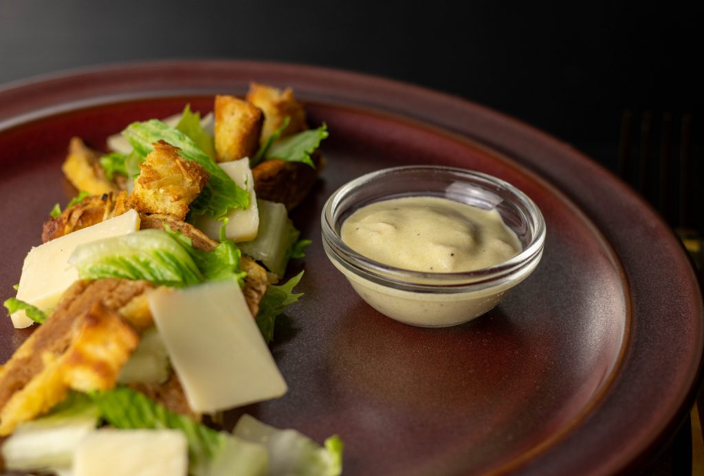 Caesar Dressing in einer kleinen Schale auf einem Teller mit Caesar Salat.