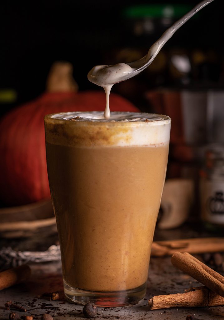 Pumpkin Spice Latte. Cremiger, herbstlicher, würziger Kaffee. Creme läuft von einem Löffel in das Glas.