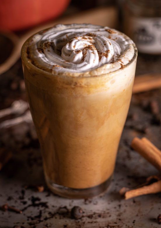 Pumpkin Spice Latte mit Sahnehaube und Gewürzen in einem Glas