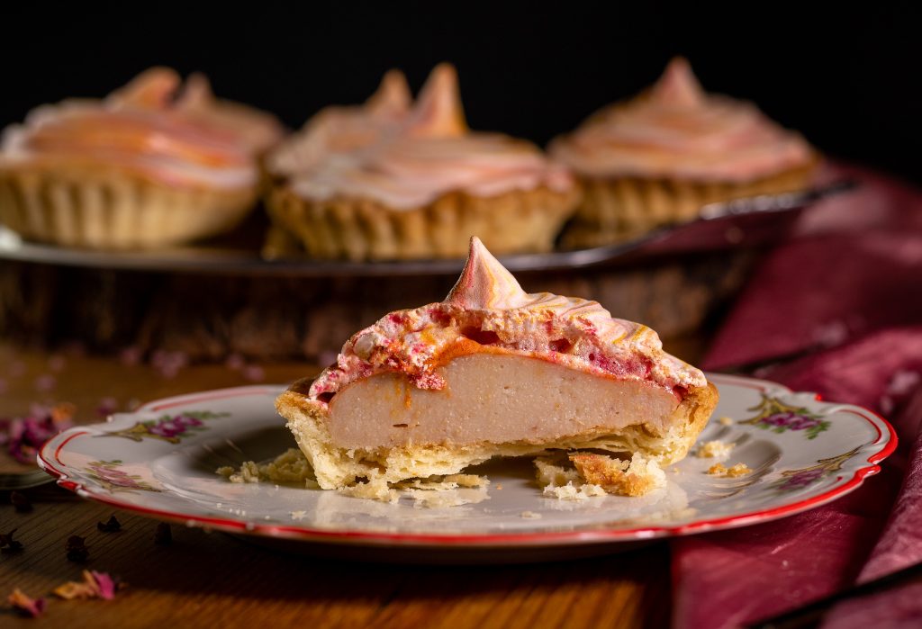 Mispeltarts mit Baiserhaube, Mispelfruchtschicht und Mürbeteigboden. Eine Tarte ist in der Mitte angeschnitten und man sieht die Schichten.