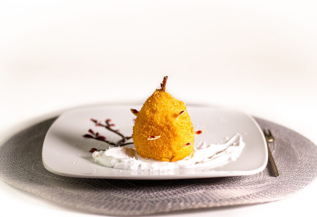 In Cider pochierte Birne. Ausgebacken im knusprigen Kokosmantel! Serviert auf duftendem Tonkaschaum und einem Schokoladen-Rotweincreme-Bäumchen.