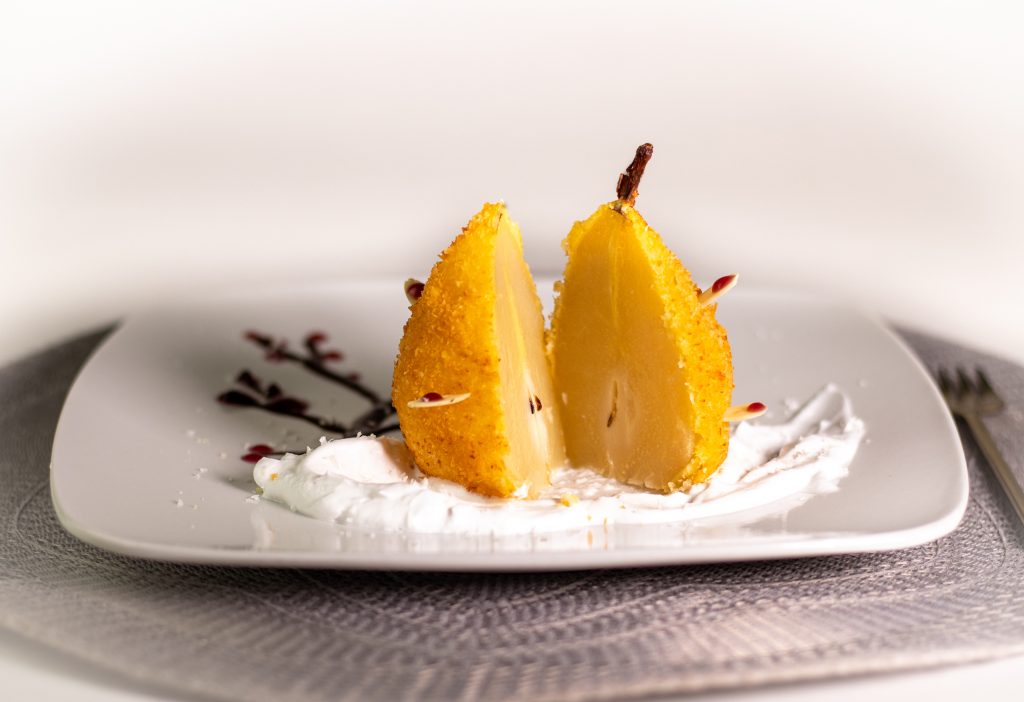 In Cider pochierte Birne. Ausgebacken im knusprigen Kokosmantel! Serviert auf duftendem Tonkaschaum und einem Schokoladen-Rotweincreme-Bäumchen.