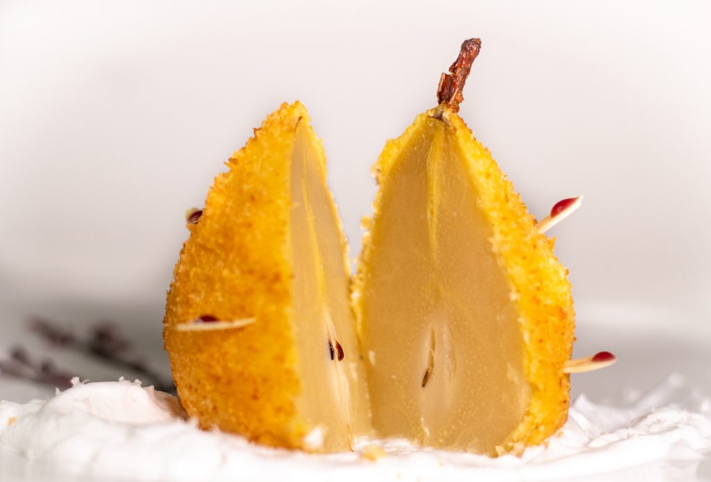 In Cider pochierte Birne. Ausgebacken im knusprigen Kokosmantel! Serviert auf duftendem Tonkaschaum und einem Schokoladen-Rotweincreme-Bäumchen.