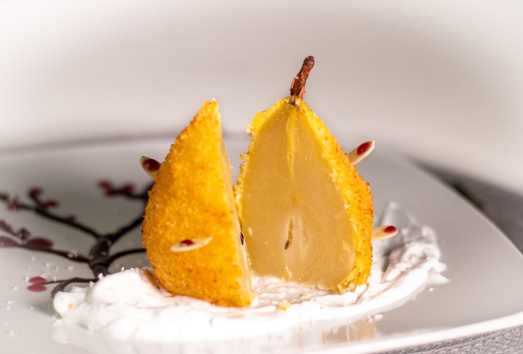 In Cider pochierte Birne. Ausgebacken im knusprigen Kokosmantel! Serviert auf duftendem Tonkaschaum und einem Schokoladen-Rotweincreme-Bäumchen.