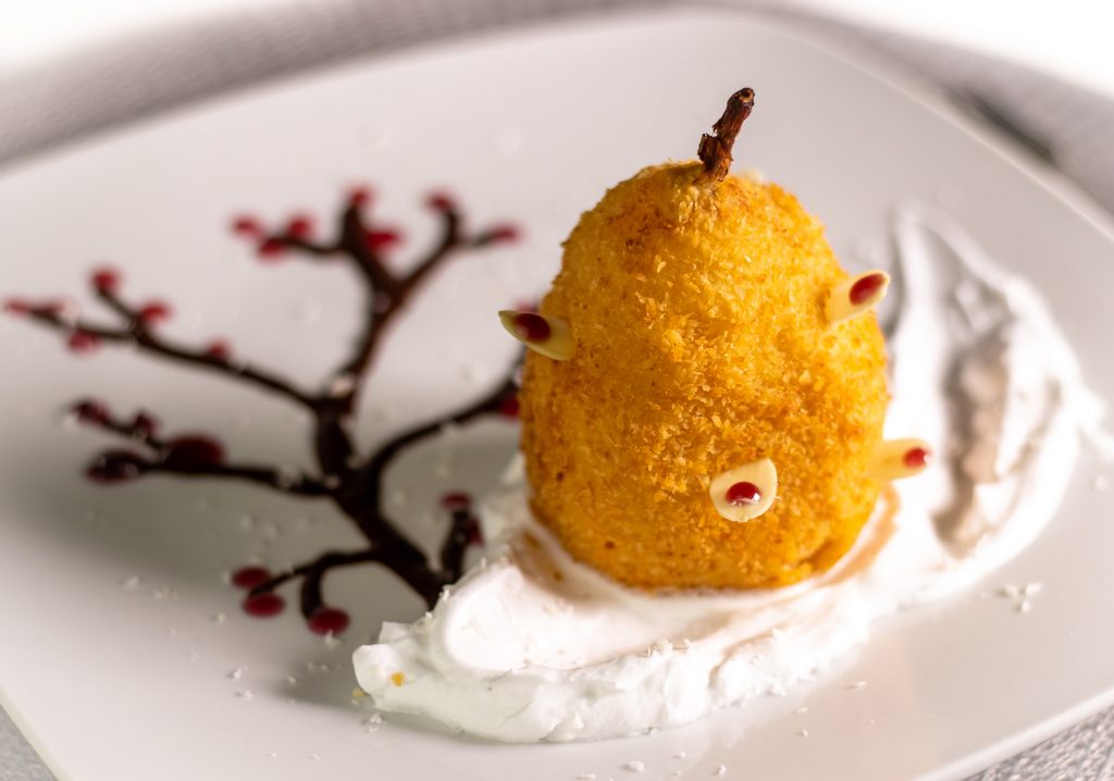 In Cider pochierte Birne. Ausgebacken im knusprigen Kokosmantel! Serviert auf duftendem Tonkaschaum und einem Schokoladen-Rotweincreme-Bäumchen.