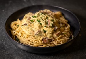 Dampfende, vegane Spaghetti alla Carbonara auf schwarezem Teller