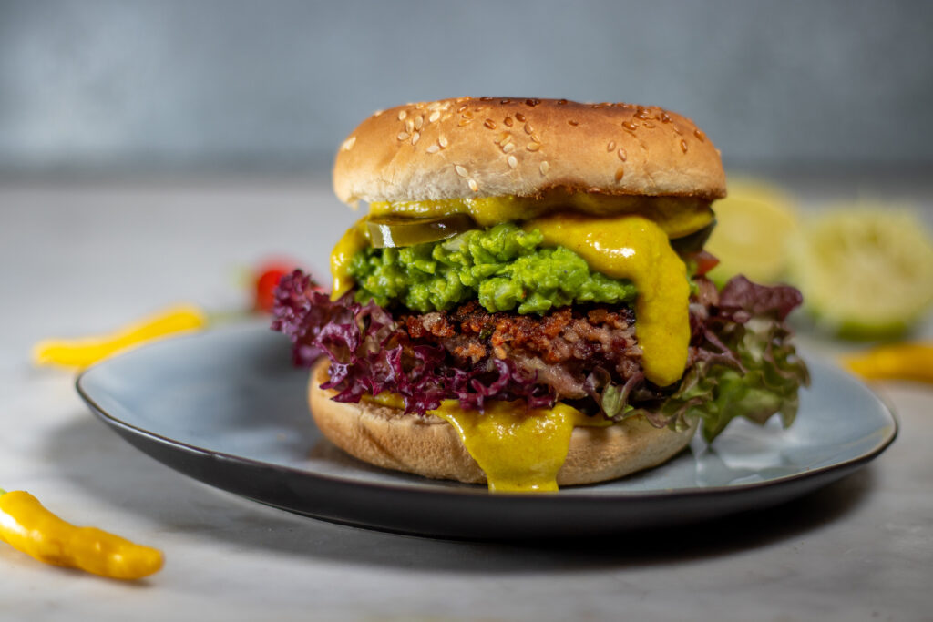 Erbsguacamole und vegane Käsesauce auf einem Black Bean Burger