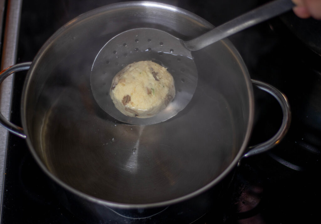 7. Die Knödel mit einer Schöpfkelle in das siedende Wasser geben und garen.