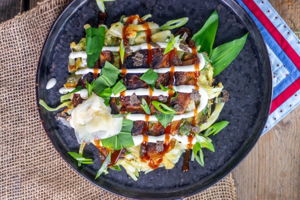 Nachdem beide Seiten des Okonomiyaki goldbraun und knusprig sind, wird es mit einer Vielzahl von Toppings garniert.