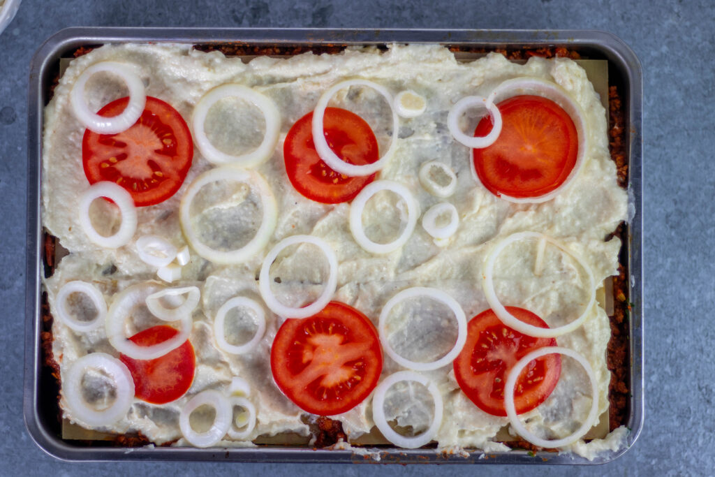 10. Die oberste Schicht der veganen Lasagne besteht aus Bechamelsauce mit Tomatenscheiben und Zwieblringen. Darauf kommt noch veganer Käse mit veganer Sahne.