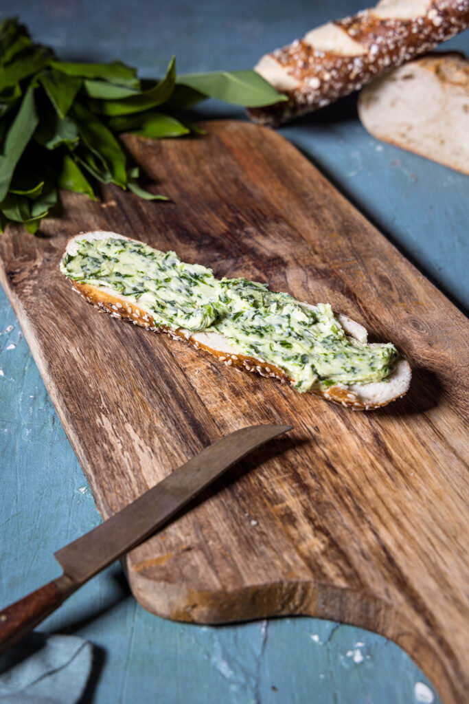 Bärlauchbutter - vegan und selbstgemacht - auf einer Laugenstange auf einem Holzbrett.