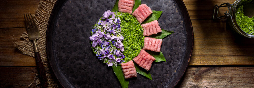 Selbstgemachte Rote Beete Gnocchi mit aromatischen Bärlauchpesto, mit essbaren Blüten angerichtet.