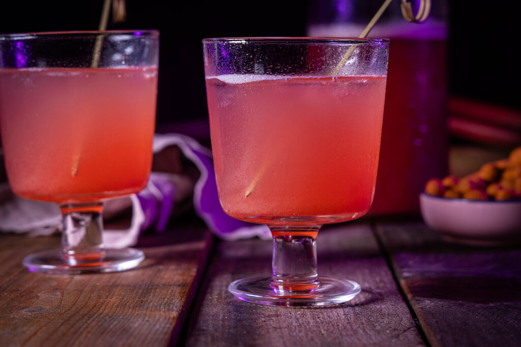 Zwei Glser mit Rhabarber-Ingwer-Bitter-Sirup als Limonade mit Sprudelwasser. Im Hintergrund eine Flasche Sirup.
