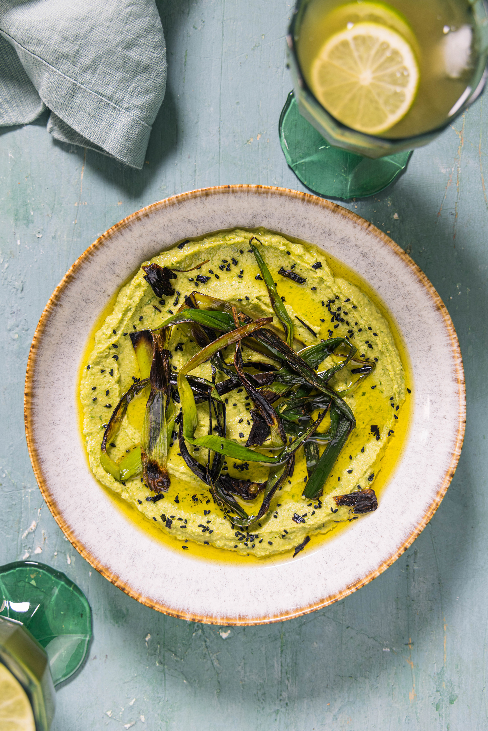 Bärlauchhummus in einer Schale mit gegrilltem Lauch. Daneben Getränke.