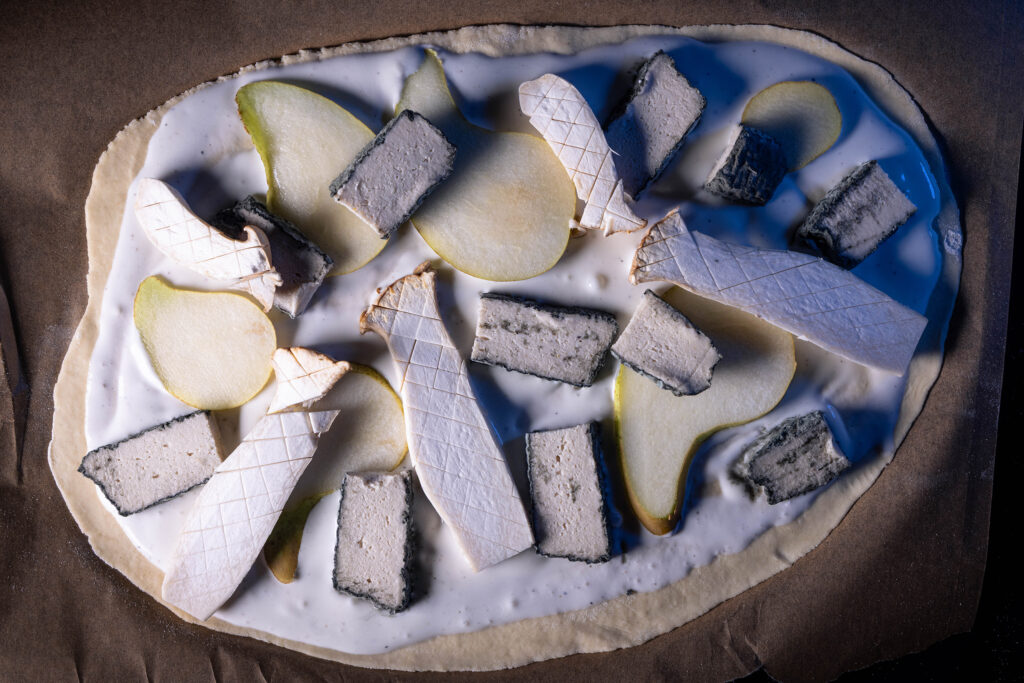 Ein roher Flammkuchen, belegt mit Kräuterseitlingen, Birnen und veganem Blauschimmelkäse