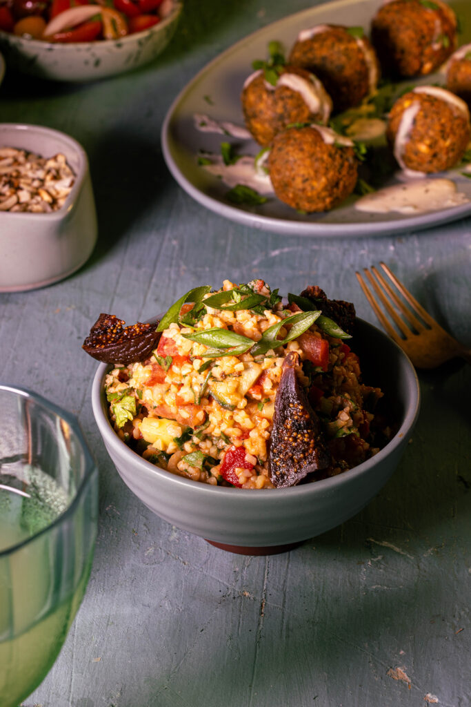 Bulgursalat in iner Schale, dahinter Falafel, geröstete Nüsse und Tomatensalat.
