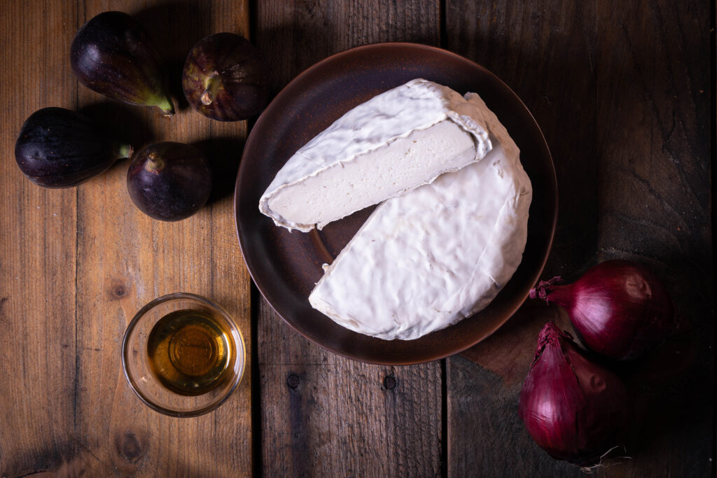Veganer Camembert, frische Feigen, rote Zwiebeln und selbstgemachter Löwenzahnhonig auf einem Holztisch.