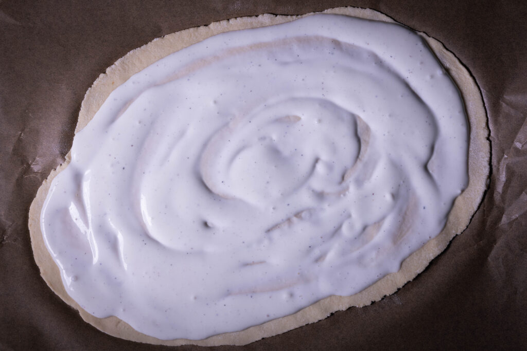 Flammkuchenteig bestrichen mit heller Sauce.