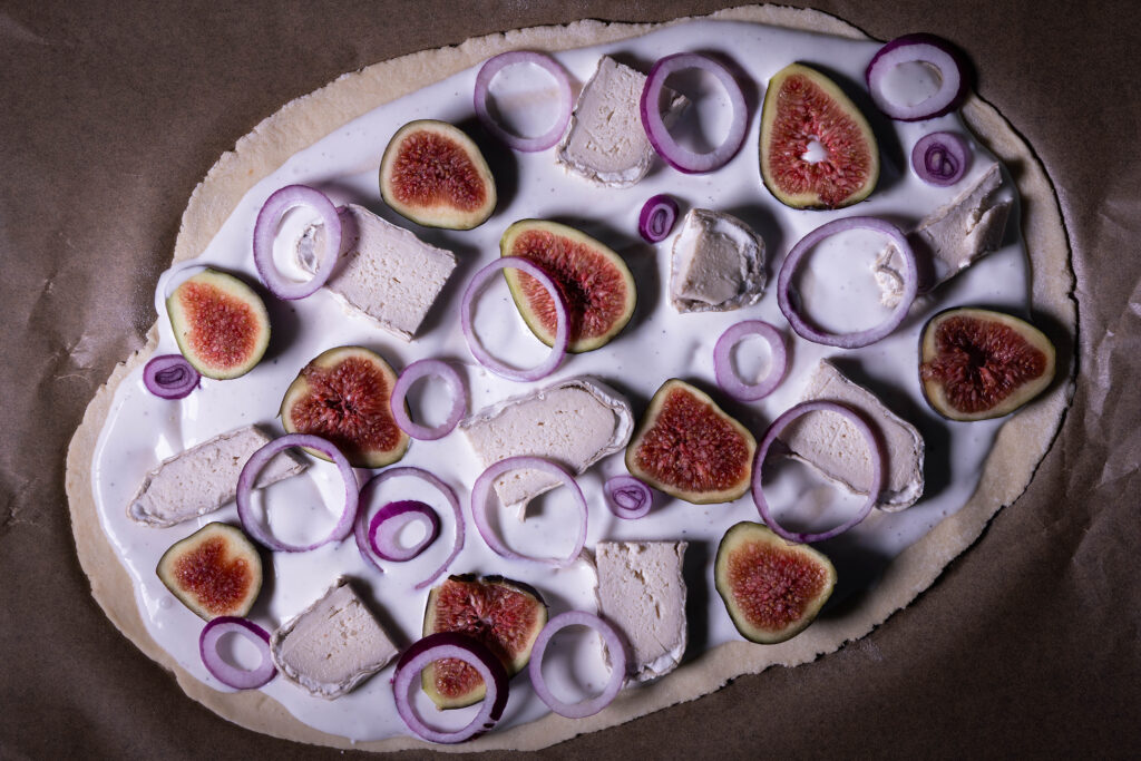 Ein roher Flammkuchen. belegt mit veganem Camembert, Feigen und roten Zwiebeln.