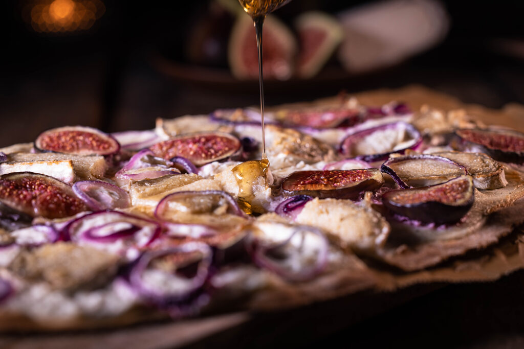 Veganer Flammkuchen mit Camembert und Feige wird mit Löwenzahnhonig beträufelt.