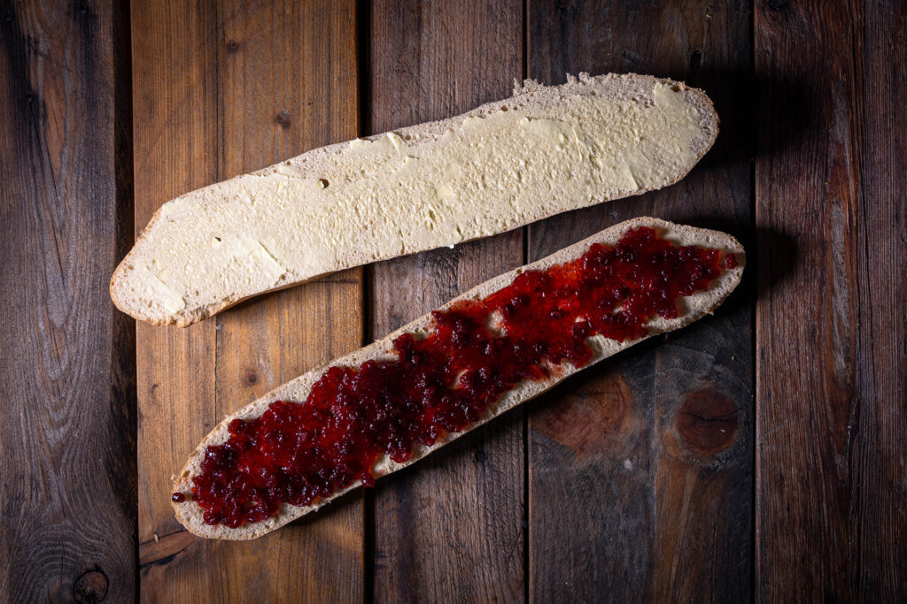 Zwei Baguettehälften. Eine mit veganer Butter bestrichen, die andere mit Preiselbeermarmelade belegt.
