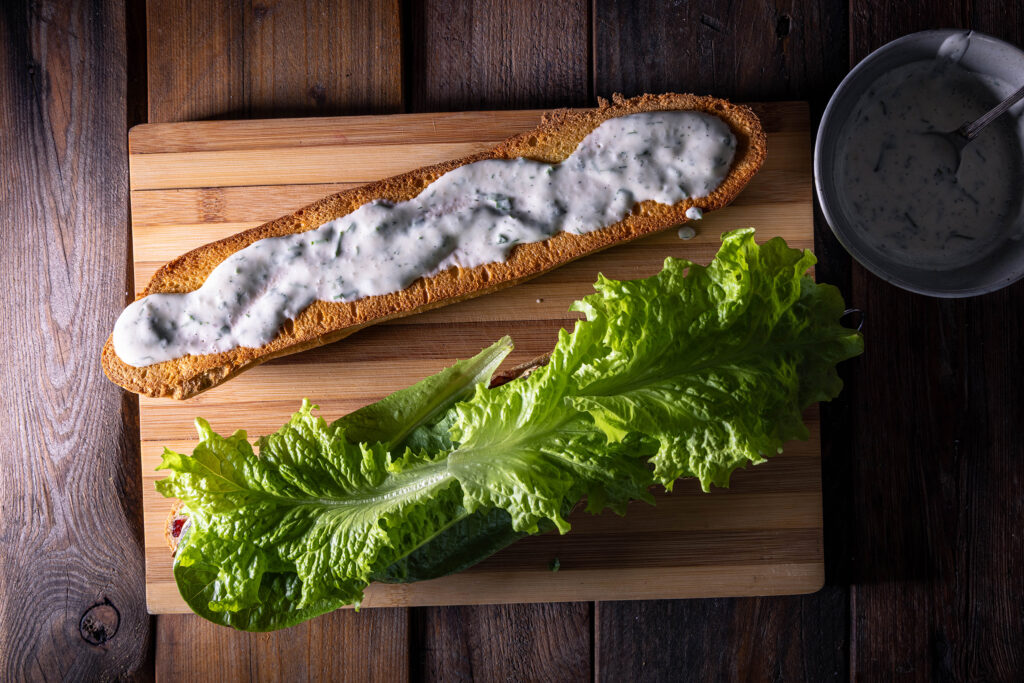 Zwei geröstete Baguettehälften. Eine ist mit Spezialsauce bestrichen, die andere mit Salat belegt.