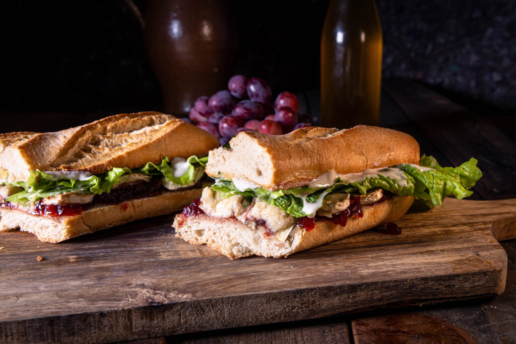 Croque Camembert - selbstgebacken und vegan - auf einem Holzbrett, dahinter rote Weintrauben.