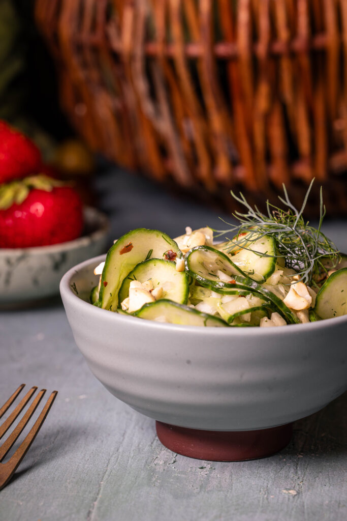 Gurkensalat mit Kokoskefirdressing - in einer Schale, dahinter eine Schälchen Erdbeeren und ein Korb