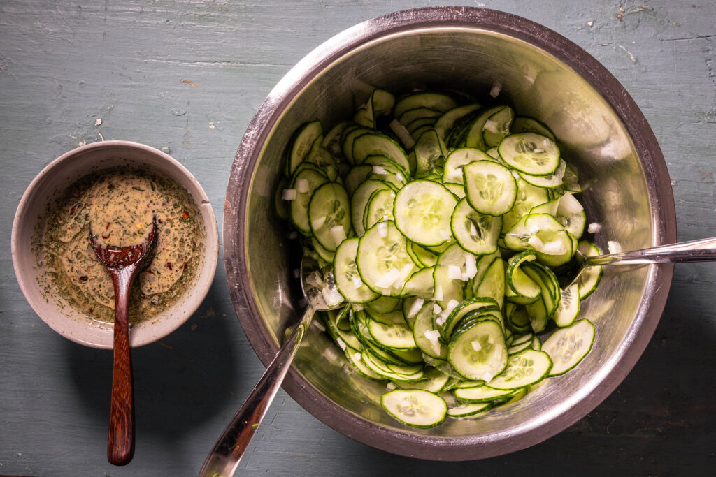 Eine Schale mit geriebener Gurke und fein geschnittener Zwiebel und eine Schale mit Dressing