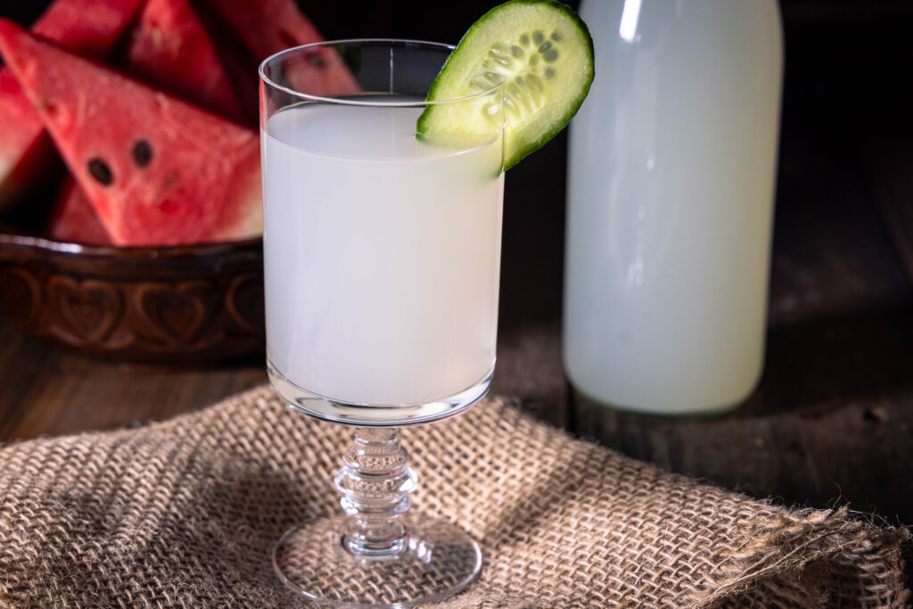 Ein Glas mit Wasserkefir und einer Scheibe Gurke.