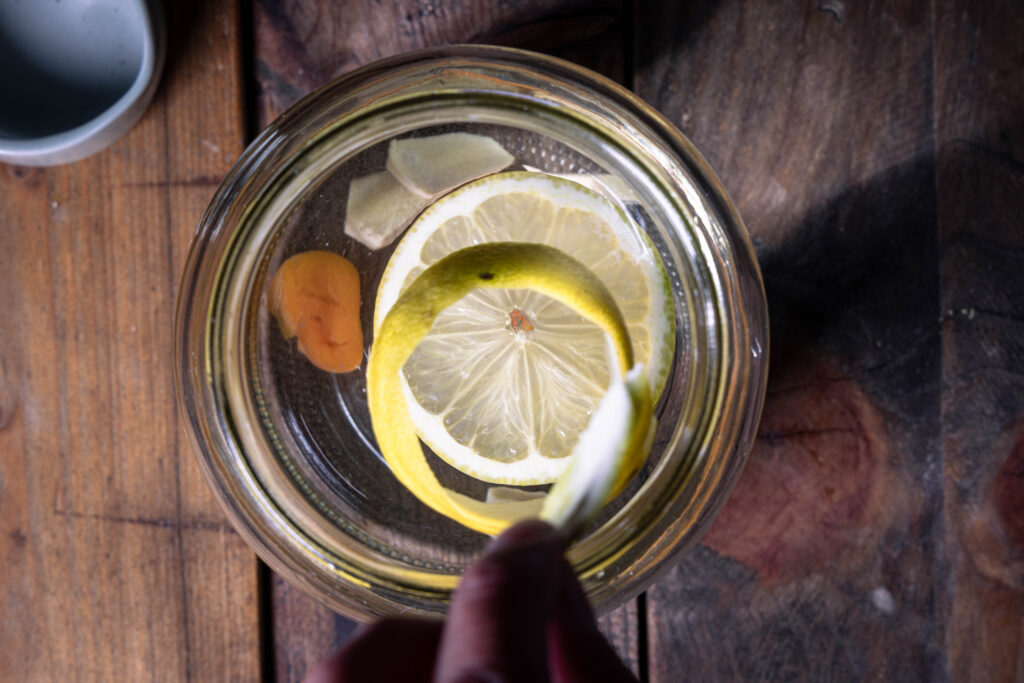 Ein großes Glas mit Zuckerwasser, Trockenobst, Zitrone und Zitronenschale darin.