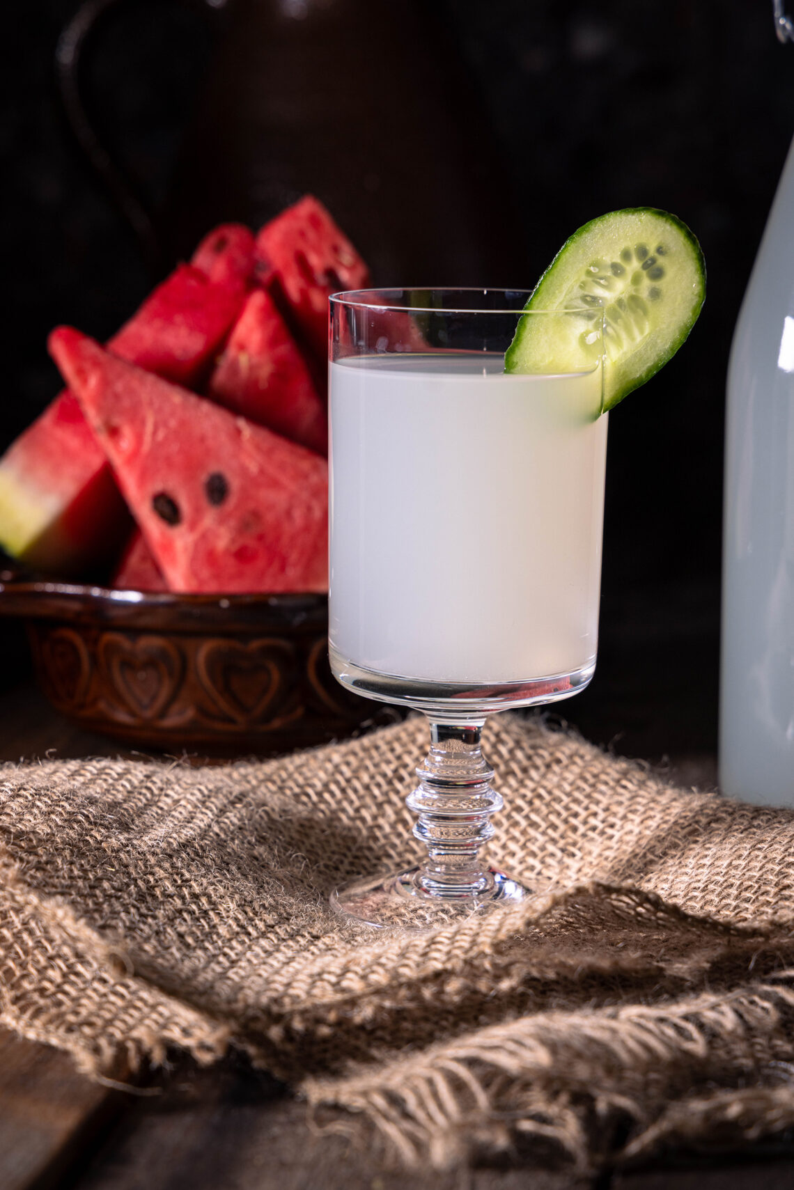 Ingwer-Bitterlemon-Kefir - in einem Glas mit Gurkenscheibe, dahiner Melonenstücke.