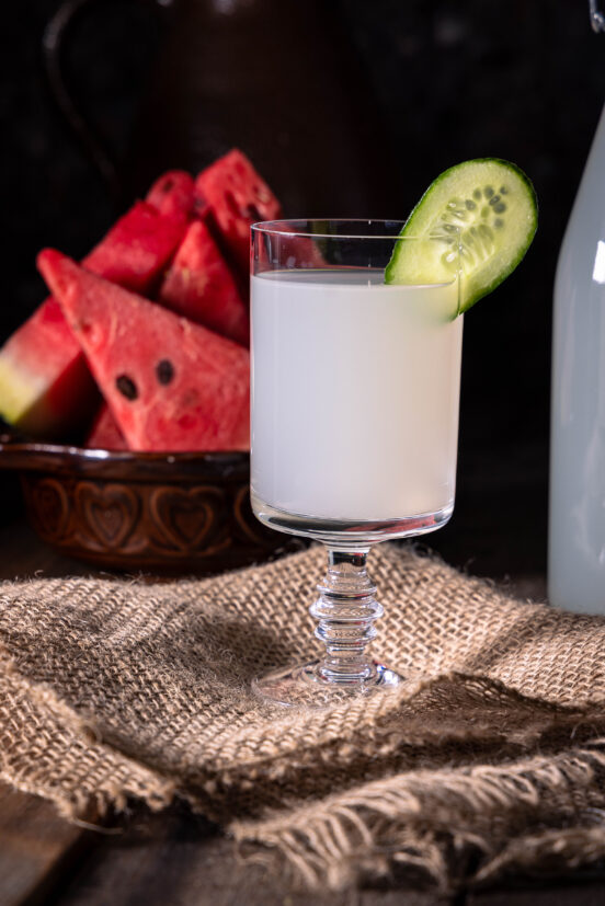 Ingwer-Bitterlemon-Kefir - in einem Glas mit Gurkenscheibe, dahiner Melonenstücke.