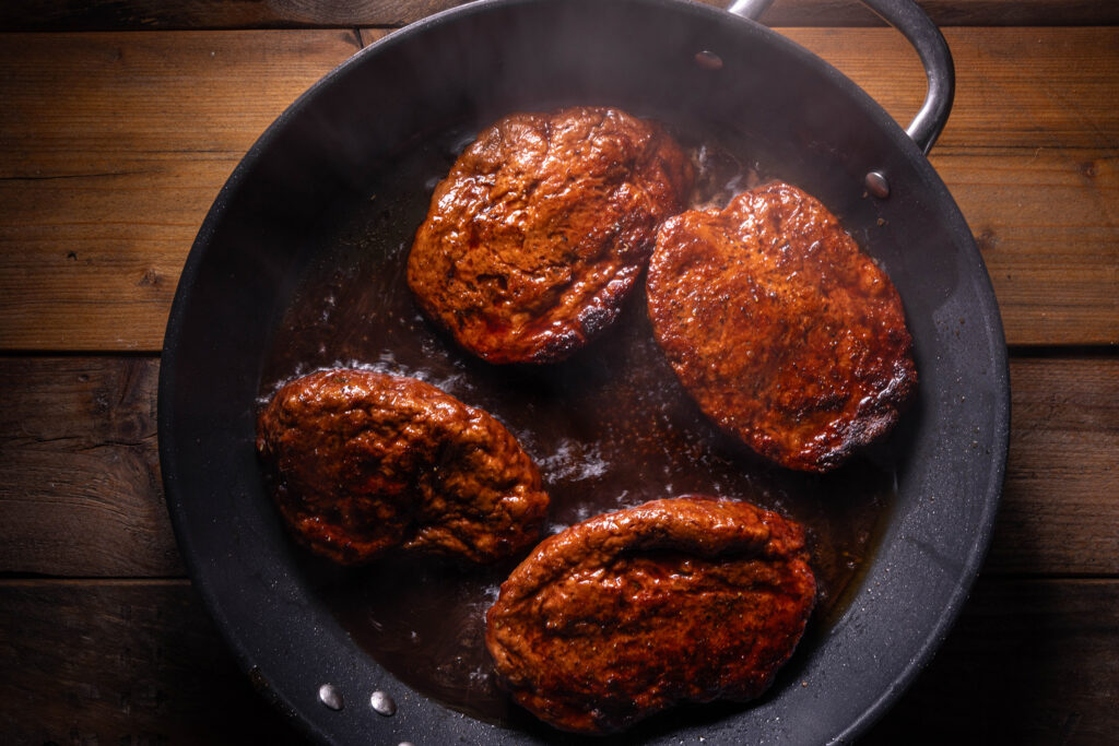 Vier Seitanfilets braten in Portweinglasur in einer Pfanne.