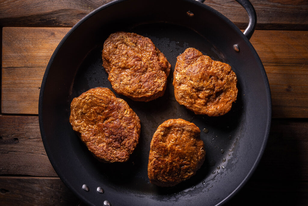 Vier rohe Seitanfilets werden in einer Pfanne angebraten.