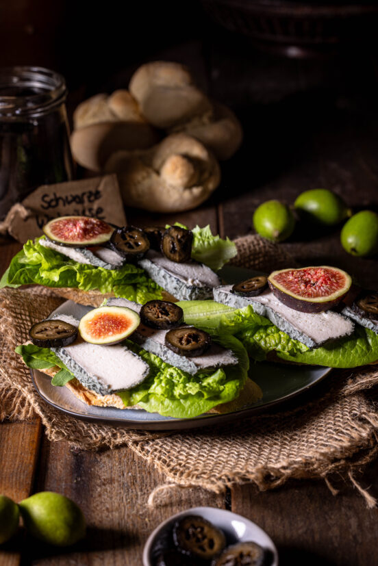 Schwarze Nüsse - eine Delikatesse aus grünen Walnüssen - hier mit Feigen auf veganem Blauschimmelkäse zu sehen.