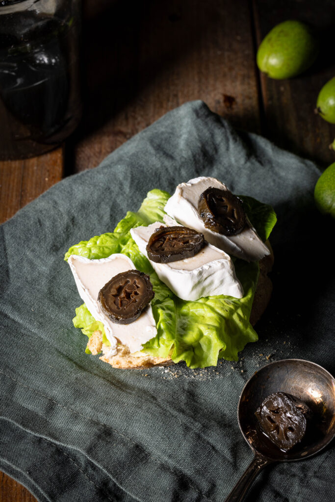 Süß-sauer eingelegte Schwarze Nüsse - aus grünen Walnüssen. Hier auf veganem Camembert.