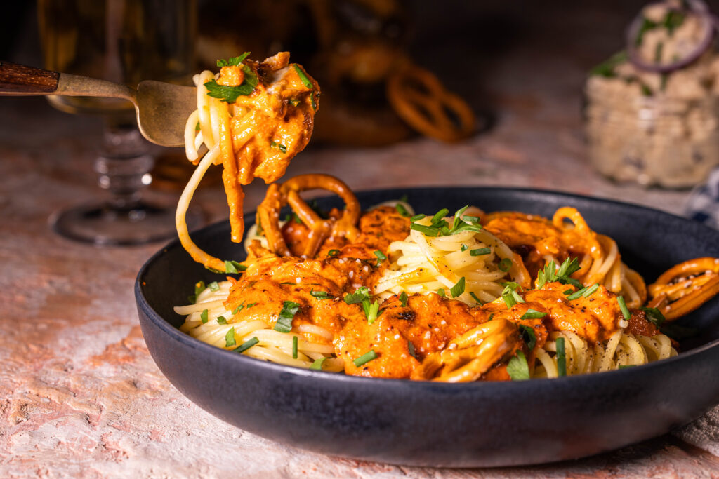 Spaghetti al Camembert – Pasta mit Obazda-Sauce. Auf einem Teller mit kleinen Brezeln. Und auf einer Gabel aufegerollt.